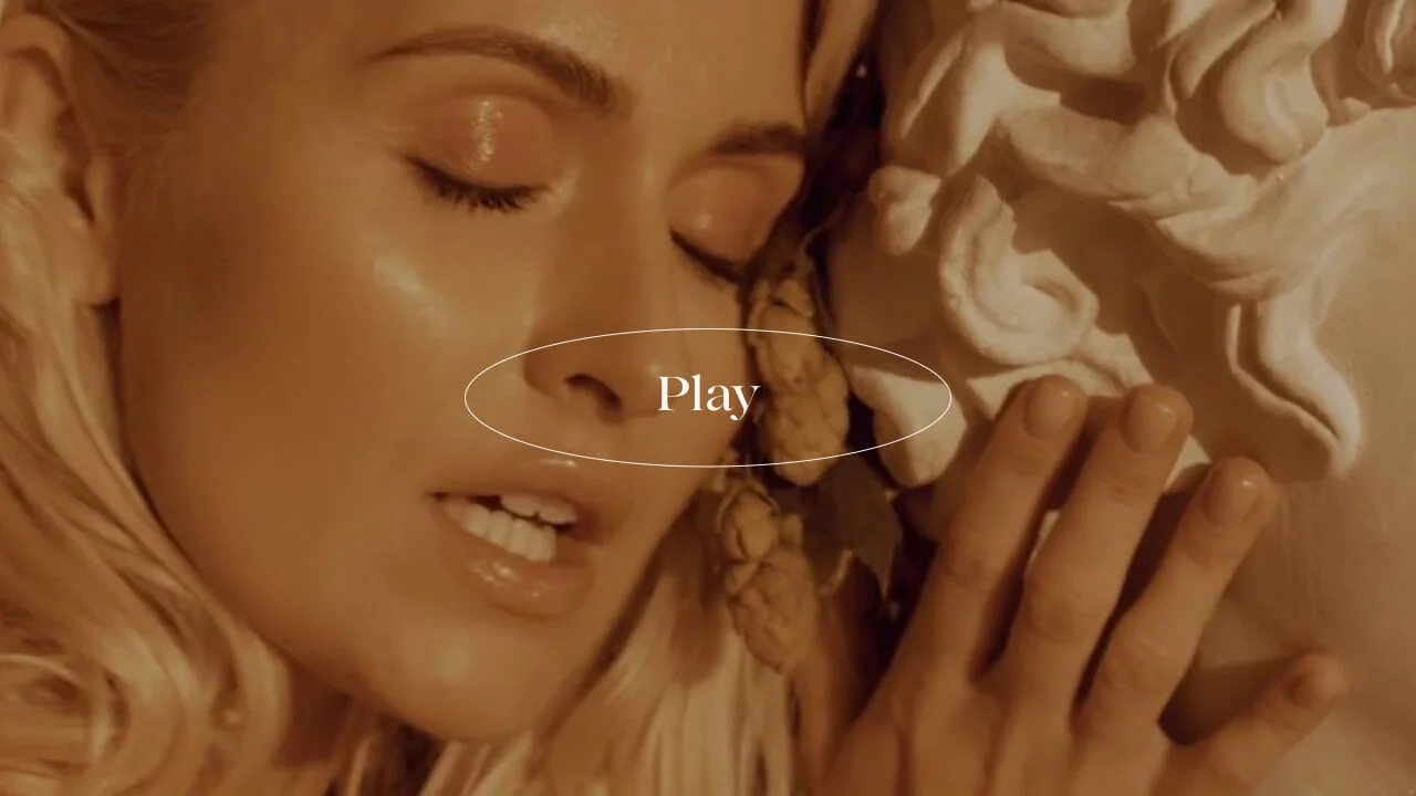 A woman with closed eyes leans against a white classical statue, her hand touching its face. The word "Play" is centered over the image.